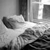 A bed is unmade near a window.