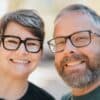 A smiling couple wearing glasses outdoors