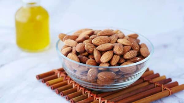 Close-up of almonds in a glass bowl next to a bottle of oil on a bamboo mat.