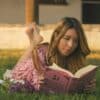 Woman enjoys a book while lounging in the grass.