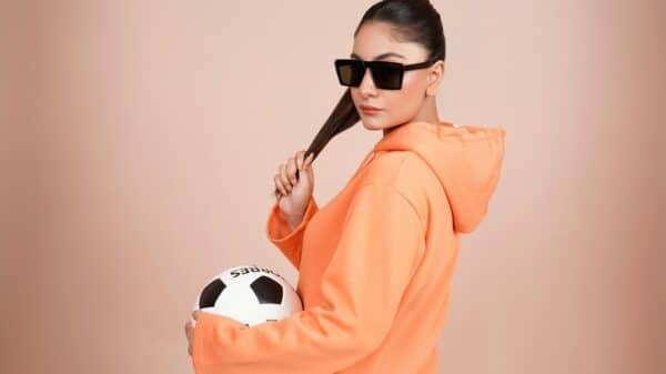 a woman in an orange hoodie holding a soccer ball