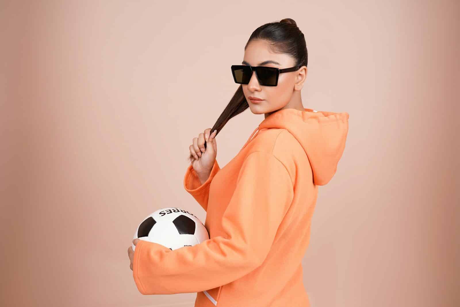 a woman in an orange hoodie holding a soccer ball