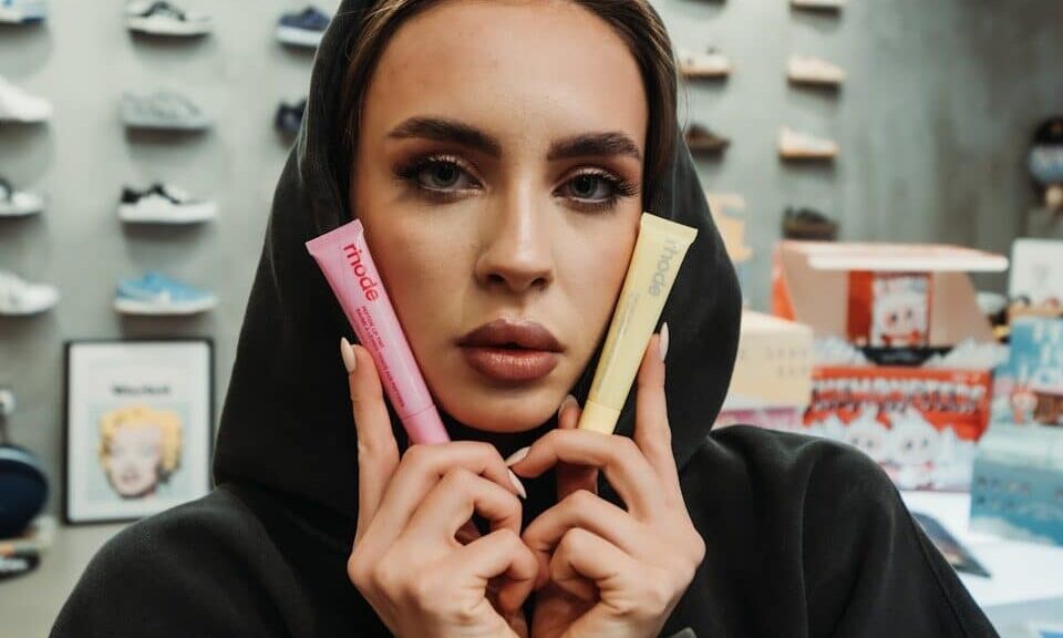 Woman in hoodie holds pink and yellow tubes