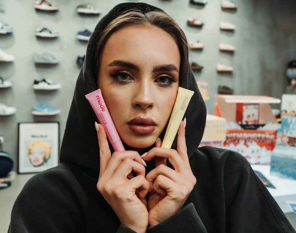 Woman in hoodie holds pink and yellow tubes