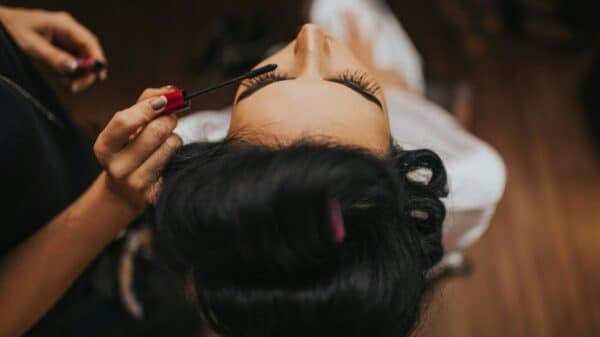 person putting mascara to a woman wearing white top